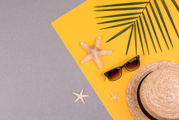 óculos e chapéu com conchas e estrelas do mar em uma superfície colorida