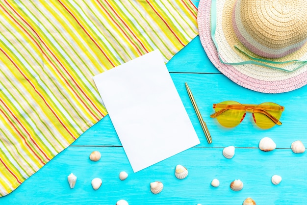 Óculos e chapéu para as férias de verão em um fundo azul. bloco de notas e canetas esferográficas rodeadas de conchas e acessórios de verão. vista do topo. copie o espaço.