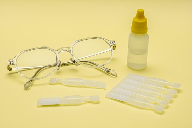 Foto Óculos e colírios descartáveis isolados em fundo amarelo
