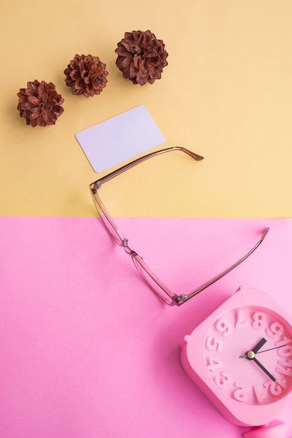 Óculos elegantes sobre fundo pastel. cartão de visita, rosa pastel e cores amarelas. despertador, flores de árvore de abeto.