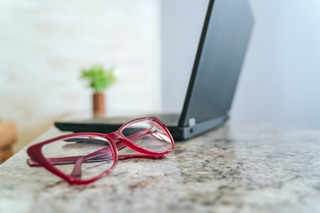 Óculos emoldurados vermelhos na mesa e laptop no fundo