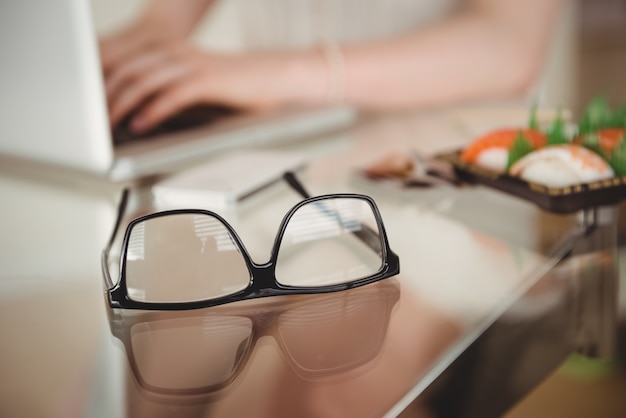 Foto Óculos na mesa contra mulher usando laptop