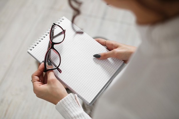 Óculos para visão e um caderno nas mãos de uma jovem.