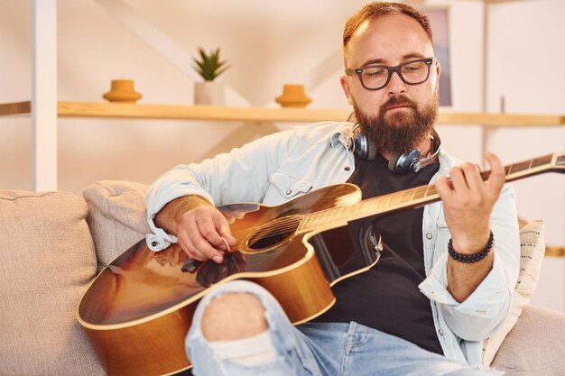 Ocupación creativa El hombre con ropa informal y con guitarra acústica está en el interior