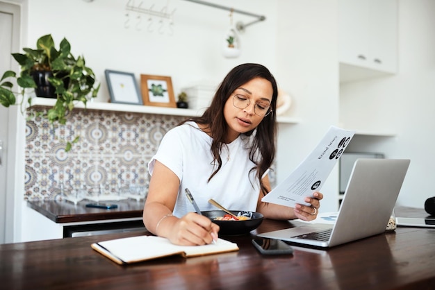 Ocupada construyendo su marca desde casa Foto de una mujer joven revisando papeleo y escribiendo notas mientras trabaja desde casa