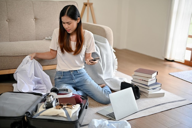 Una ocupada mujer asiática está preparando sus pertenencias y empacando su equipaje en su sala de estar