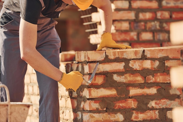 Ocupado com parede de tijolos Trabalhador da construção em uniforme e equipamento de segurança tem emprego na construção