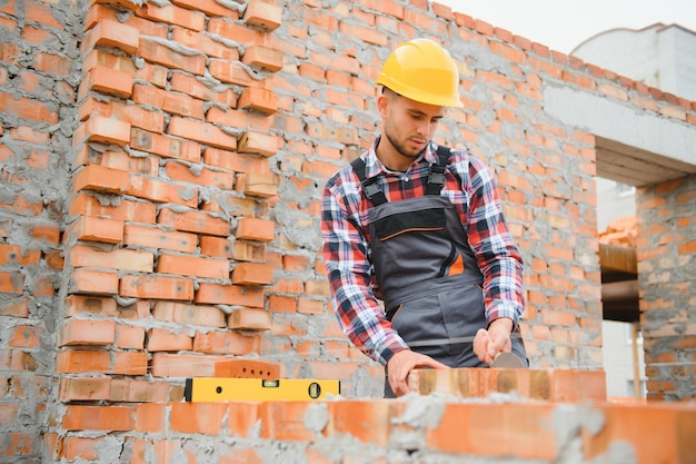 Ocupado com parede de tijolos Trabalhador da construção em uniforme e equipamento de segurança tem emprego na construção