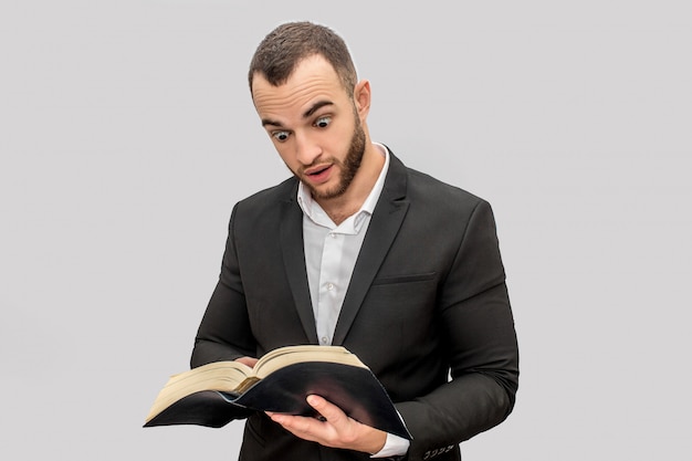 Ocupado y concentrado joven en traje de pie y leer el libro. Él lo señala. Guy usa traje.