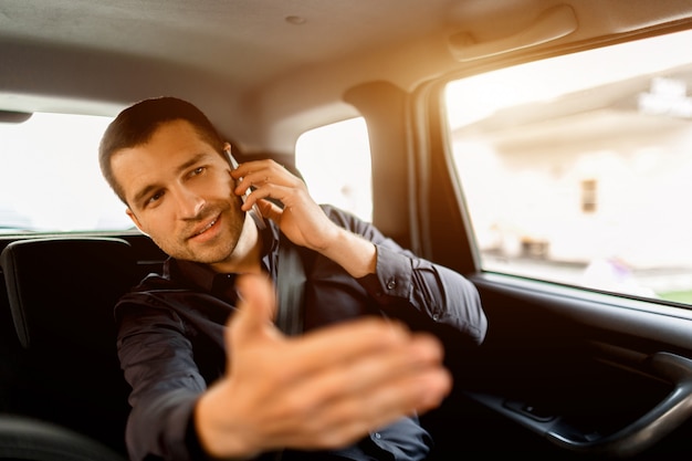 Ocupado hombre de negocios en un taxi. Concepto de multitarea El pasajero viaja en el asiento trasero y trabaja simultáneamente. Habla en un teléfono inteligente y se comunica con el conductor