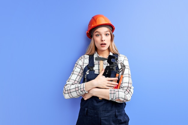 Ocupado ingeniero constructor mujer mirando a cámara con expresión de sorpresa sosteniendo en la mano herramientas ajustables