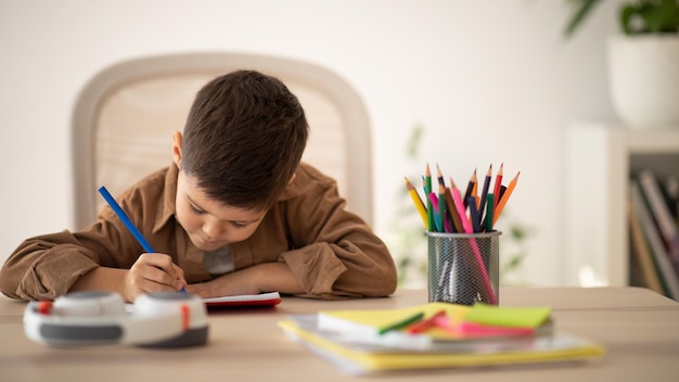 Foto ocupado niño pequeño europeo serio dibujar escribir estudiar en la mesa en la sala de estar