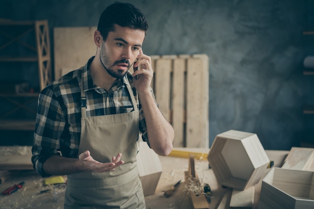 Ocupado, preocupado, sobrecargado, capataz, personal de mantenimiento, habla en un teléfono inteligente, tiene problemas con los clientes, decide ofertas, construcción de muebles, restauración, reparación, pedidos en casa, lugar de trabajo