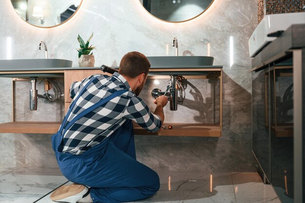 Foto ocupado reparando sifón fontanero en uniforme azul está trabajando en el baño