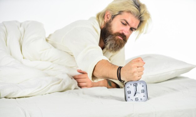 Odio despertar temprano en la mañana Chico somnoliento y despertador en la cama Hombre barbudo con despertador Hipster quiere dormir Horario Acostarse a tiempo Levántate ahora mismo Despertador de hombre estresado