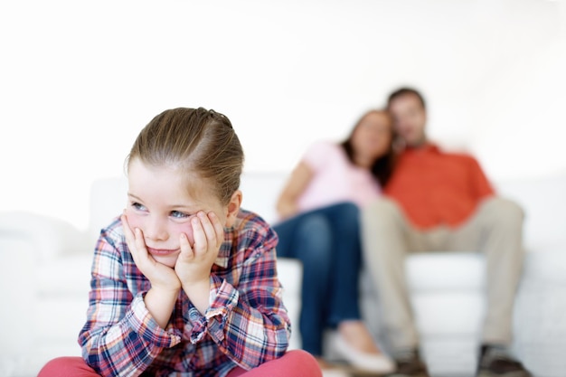 Odio el tiempo de espera Una niña pequeña se sienta y se enfurruña mientras sus padres en el fondo