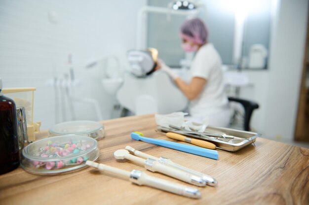 Foto odontologia. prática dental. ferramentas dentais modernas, instrumentos de aço inoxidável esterilizados em uma superfície de madeira contra um fundo desfocado de um dentista tratando cáries em um paciente em um consultório odontológico