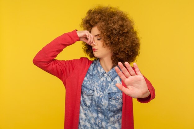 Foto odor horrível retrato de mulher confusa com cabelo encaracolado, beliscando o nariz para evitar o mau cheiro e mostrando o gesto de parada expressando repulsa nojo interior tiro de estúdio isolado em fundo amarelo