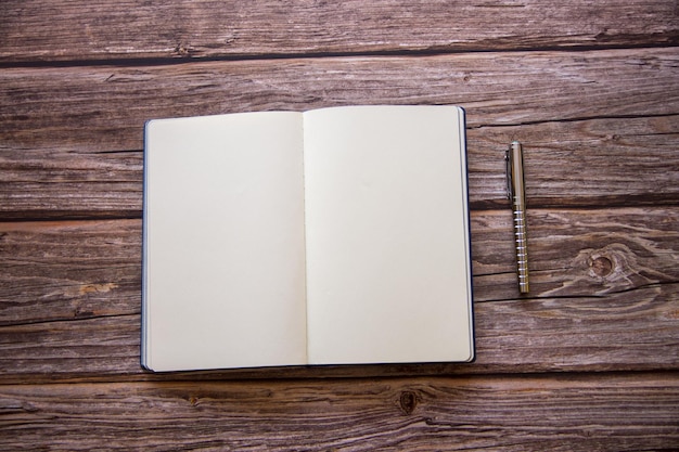 Öffnen Sie ein leeres weißes Notizbuch mit einem Stift auf einem Holzschreibtisch