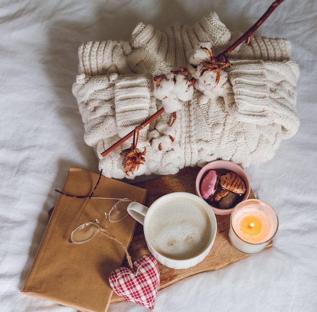 Öko-Dekor für zu Hause. Gemütliche Einrichtung zu Hause. Eine Tasse Cappuccino, Kekse, eine Kerze auf dem Bett. Wintermorgen. Ferien.