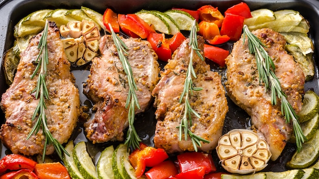 Ofen backte Schweinefleisch Entrecotes mit grünem Pfeffer und Zucchini auf Backblech, auf einem dunklen Hintergrund.