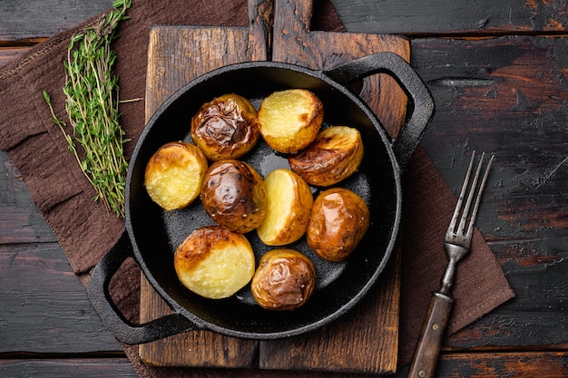 Ofenkartoffeln, in Bratpfanne aus Gusseisen, auf altem dunklem Holztischhintergrund, Draufsicht flach