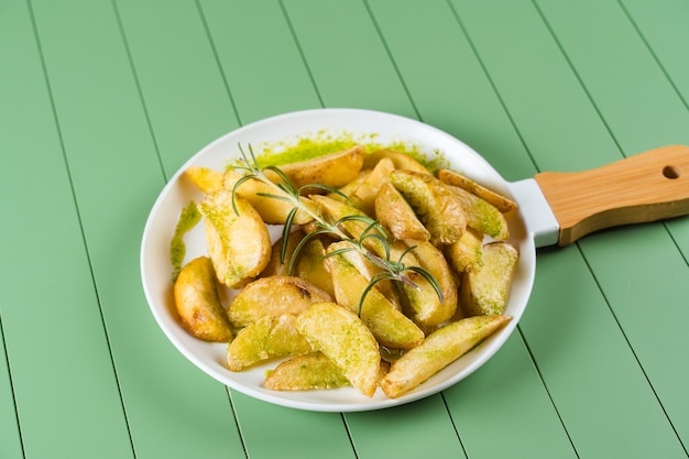 Ofenkartoffeln mit grüner Sauce und Rosmarin auf einem weißen Teller in Form einer Pfanne. Bratkartoffeln mit Pesto-Sauce auf einem grünen Tisch.