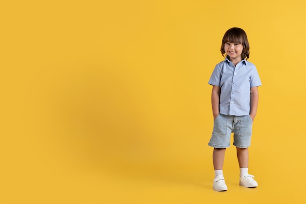 Oferta especial para niños Adorable niño pequeño con las manos en los bolsillos sonriendo a la cámara fondo amarillo espacio vacío