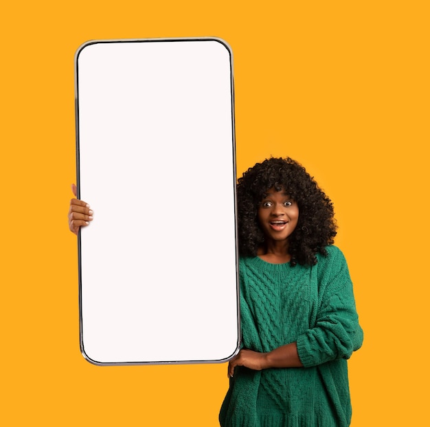 Oferta en línea emocionada dama afroamericana sosteniendo un gran teléfono inteligente en blanco en la mano