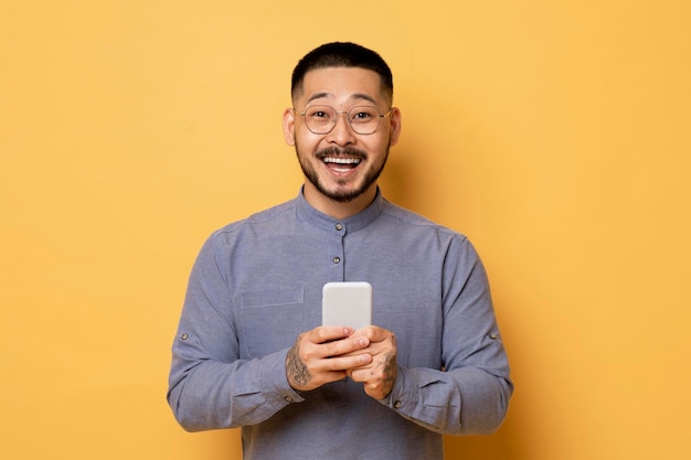 Oferta móvil emocionado joven asiático sosteniendo teléfono inteligente y mirando a la cámara