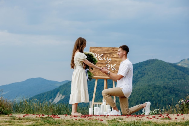 Oferta nas montanhas Um cara coloca um anel em sua noiva enquanto está de joelhos Casal feliz Casa comigo Boa sorte com a proposta