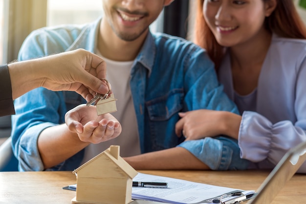 Foto oferta representativa closeup mano ofrece el llavero de la casa a la joven pareja asiática