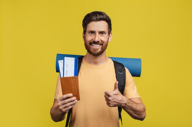 Ofertas de vuelos baratos Hombre feliz sosteniendo boletos con pasaporte gesticulando con el pulgar hacia arriba de pie con mochila