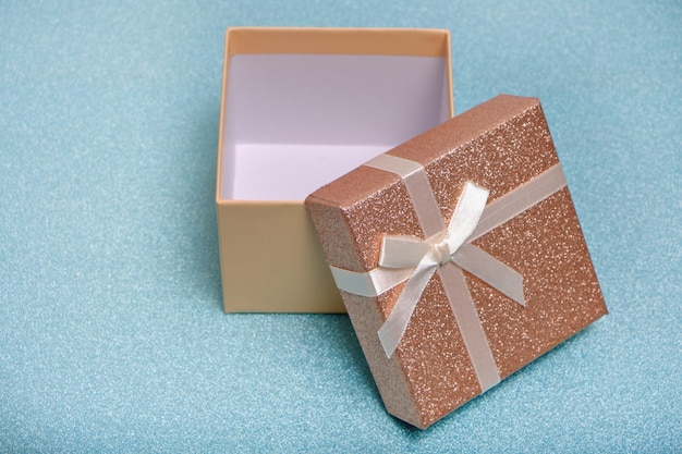Offene Geschenkbox mit beigem Band und Schleife auf glänzendem Hintergrund