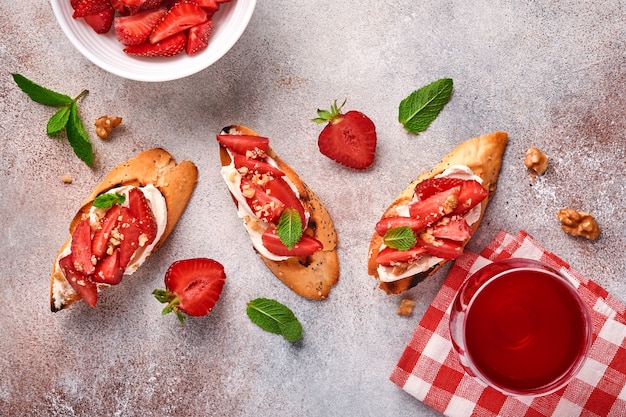 Offene Sandwiches mit Erdbeeren, Weichkäseminze und Walnuss in Keramikplatte auf hellgrauem Steinhintergrund. Sommer und gesunde Ernährung, vegetarisches Lebensmittelkonzept. Ansicht von oben.