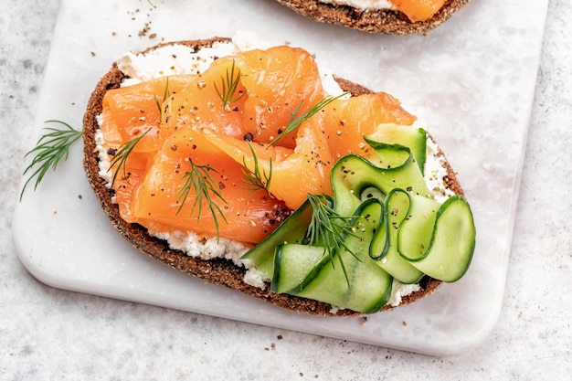 Offene Sandwiches mit Roggenbrot mit gesalzenem Lachs und Gurke auf einem weißen Steintisch Gesunde Ernährung