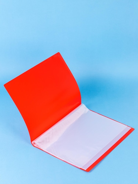 Offener roter Aktenordner aus Kunststoff mit leerem Blatt Papier, isoliert auf blauem Grund, Nahaufnahme