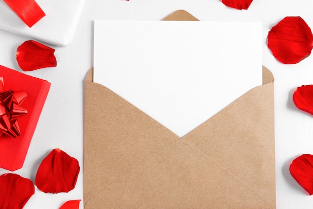 Offener Umschlag mit Liste auf weißem Holztisch mit roten Rosenblättern und Draufsicht der Geschenkboxen