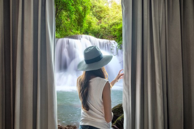 Offener Vorhang der jungen Frau, um schönen Wasserfall zu sehen, der mit Sonnenlicht natürlich fließt