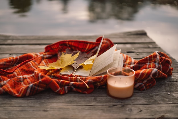 Offenes Buch mit Kerze und Strauß Herbstblätter mit einem Plaid auf Holzhintergrund