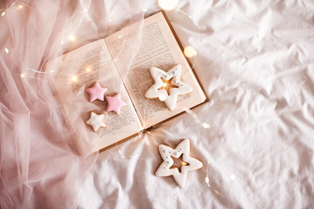 Offenes Buch mit Lebkuchen mit leuchtenden Lichtern, Nahaufnahme im Bett. Winterferienzeit. Guten Morgen. Weihnachten.