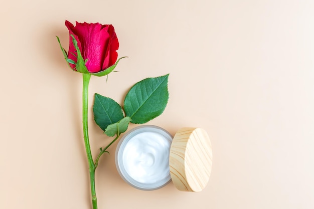 Offenes Glas mit Gesichts- oder Körpercreme mit roter Rose auf beigem Hintergrund Produktpräsentation von Hautpflege-Anti-Aging-Kosmetika