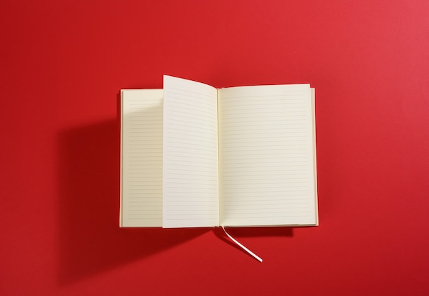 Offenes Notizbuch mit leeren weißen Blättern auf roter Oberfläche, Ansicht von oben