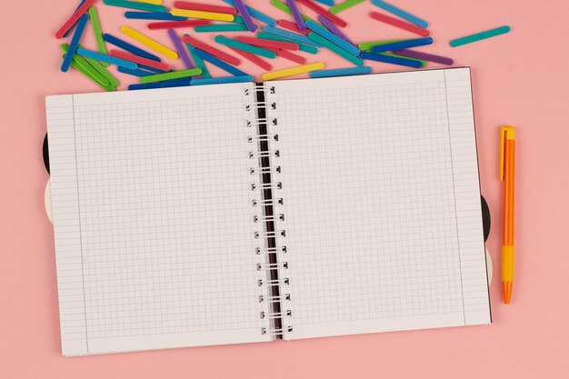 Offenes quadratisches Schulnotizbuch, Stift, bunte Mathe-Sticks auf rosa Hintergrund. Leeres weißes Blatt