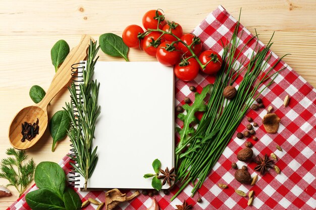 Offenes Rezeptbuch mit frischen Kräutertomaten und Gewürzen auf Holzhintergrund