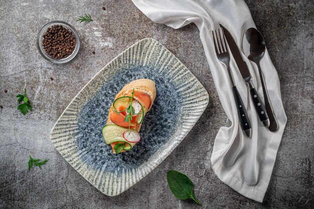 Offenes Sandwich mit Lachs, Wolfsbarsch, Gurke und Rettich auf einem grauen Steintisch