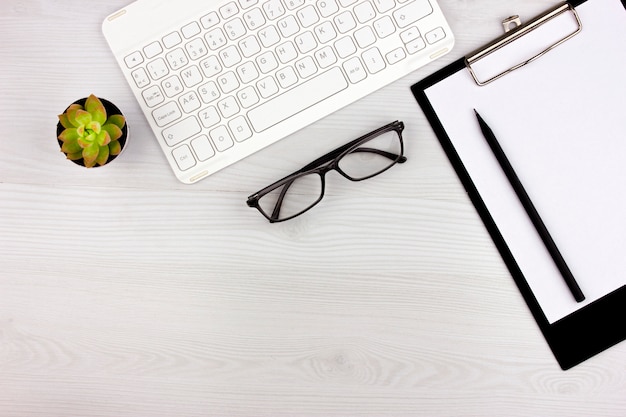 Office flatlay con teclado blanco, gafas de lectura, mascota y cuaderno