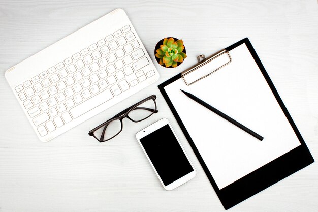 Office flatlay con teclado blanco, gafas de lectura, mascota y cuaderno