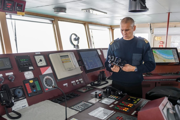 Foto offizier auf wache mit fernglas auf der navigationsbrücke kaukasischer mann in blauer uniformpullover auf der brücke eines frachterschiffs