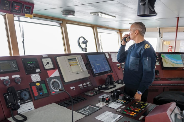 Offizier auf Wache mit Funk auf der Navigationsbrücke Kaukasischer Mann in blauem Uniformpullover auf der Brücke eines Frachtschiffs